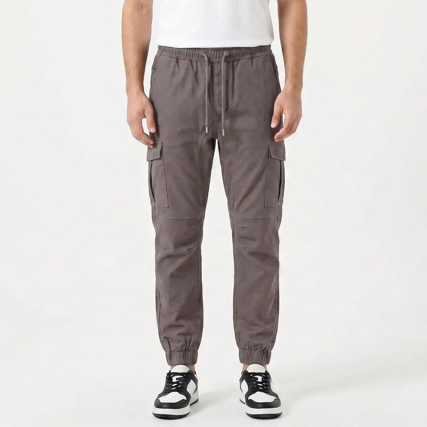 Men's slim fit cotton cargo trousers by FJØRNA, featuring multiple cargo pockets and a tailored fit in a neutral color.