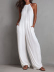 White pleated halter neck wide-leg resort jumpsuit for women by FJØRNA, shown with flowing fabric and stylish design.