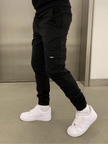 Men's black cargo jogger trousers by FJØRNA, featuring multiple pockets and a relaxed fit, shown on a model.