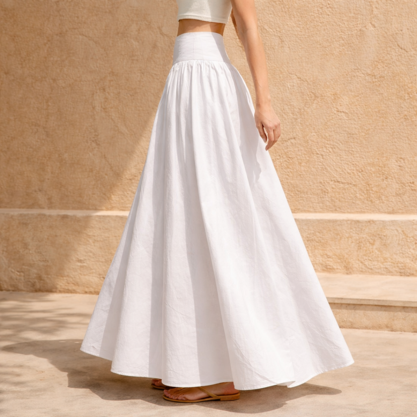White cotton high-waist maxi skirt by FJØRNA, flowing design with pleats, shown on a model with hands on hips.