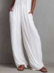White pleated halter neck wide-leg resort jumpsuit for women by FJØRNA, featuring a stylish halter top and flowing wide-leg pants.