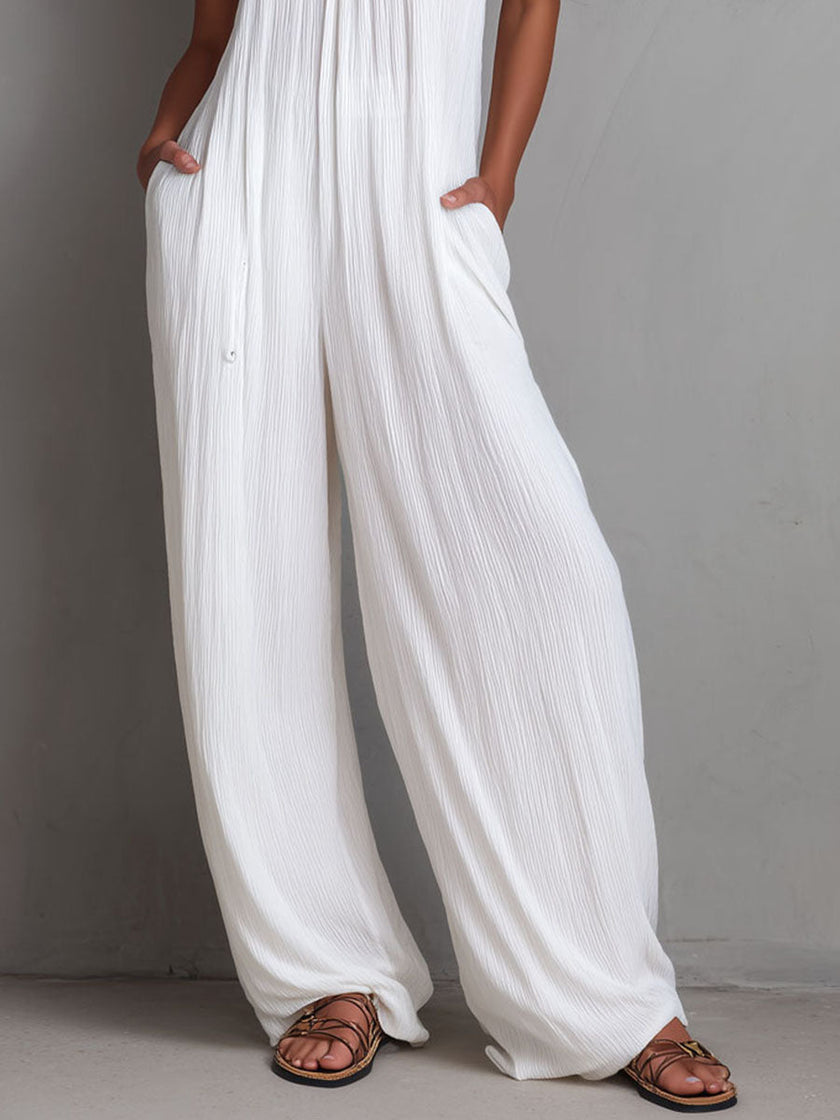 White pleated halter neck wide-leg resort jumpsuit for women by FJØRNA, featuring a stylish halter top and flowing wide-leg pants.