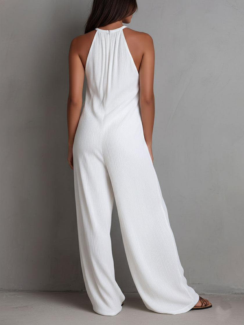 FJØRNA white pleated halter neck wide-leg resort jumpsuit worn by a woman, showcasing elegant design and flowy fabric.