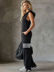 FJØRNA black sleeveless hooded jumpsuit with white vertical stripes, featuring a relaxed fit and drawstring waist for women.