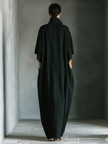 Black cotton maxi dress for women by FJØRNA, flowing style with long sleeves and a fitted waist, displayed on a hanger.