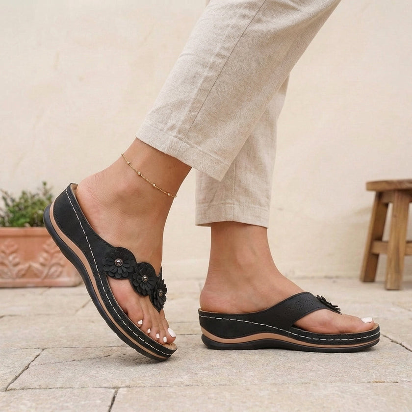FJØRNA black orthopedic open toe wedge flip-flops with floral embellishments, featuring supportive design and stylish floral accents.