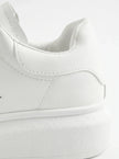 Close-up of FJØRNA men's white lace-up trainers showing minimalist design and detailed stitching on the shoes.