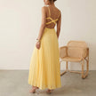 Model wearing FJØRNA elegant sleeveless maxi dress with V-neck and pleated design, showcasing flowing fabric and sophisticated style.