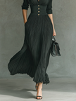 FJØRNA women's pleated maxi dress with flowing fabric and a fitted waist, shown hanging against a neutral background.