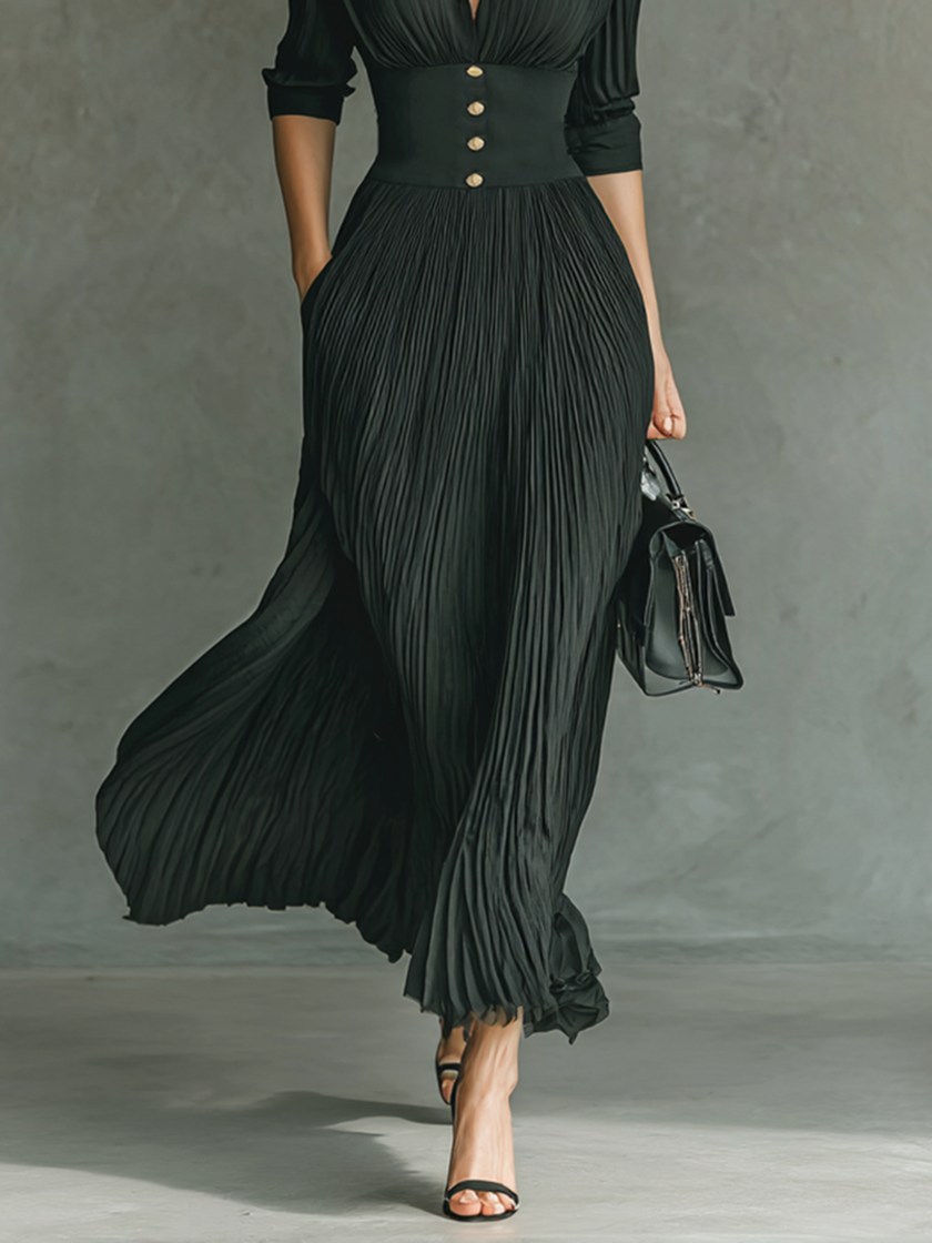 FJØRNA women's pleated maxi dress with flowing fabric and a fitted waist, shown hanging against a neutral background.