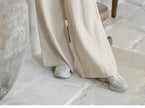 FJØRNA linen wide-leg women's trousers with a loose fit and pull-on design, shown on a model in a casual indoor setting.