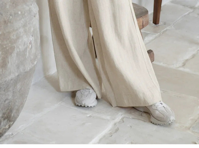 FJØRNA linen wide-leg women's trousers with a loose fit and pull-on design, shown on a model in a casual indoor setting.