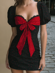 FJØRNA bold red bow polka dot mini dress with puff sleeves and fitted waist, featuring playful polka dot pattern on lightweight fabric.