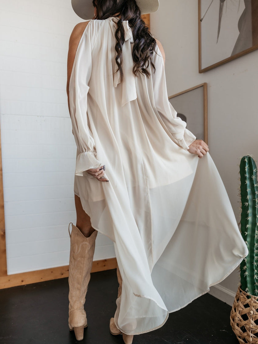 FJØRNA sleeveless maxi dress with halter neckline and asymmetric hem, flowing fabric perfect for elegant summer occasions.