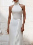 White satin pleated halter evening gown by FJØRNA with elegant design, showcasing the flowing pleats and sophisticated halter neckline.