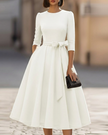 FJØRNA crew-neck A-line midi dress, elegant wedding guest dress in soft fabric, shown on a hanger with a neutral background.