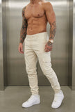 Men's cargo jogger trousers in cream by FJØRNA, shown in a relaxed fit with side pockets and elastic cuffs.