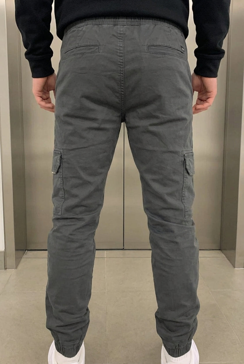 Men's grey cargo jogger trousers by FJØRNA with multiple pockets and relaxed fit, shown on a model.