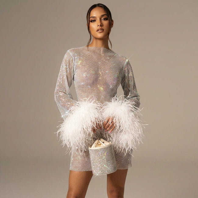 White FJØRNA sequin feather mini dress with long sleeves and sheer details, featuring sparkling sequins and feather accents.